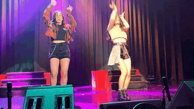 two women are dancing on stage in front of a purple curtain
