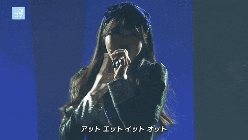 a woman singing into a microphone with chinese writing on the bottom right