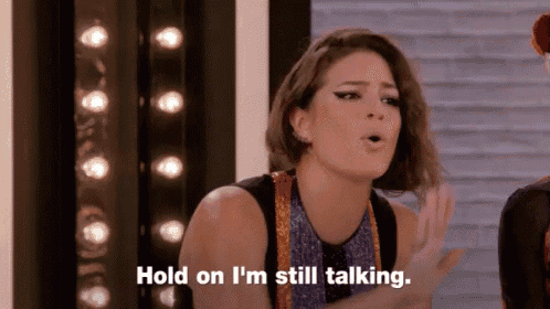 a woman is standing in front of a brick wall and saying `` hold on i 'm still talking '' .