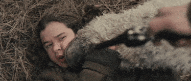 a young girl is laying in the grass with a gun pointed at her