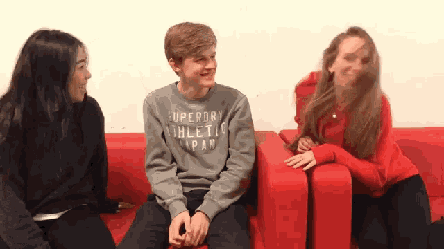 a boy in a superdry sweatshirt sits on a red couch