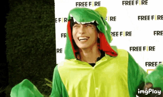 a man wearing a green dinosaur costume is smiling in front of a free fire sign