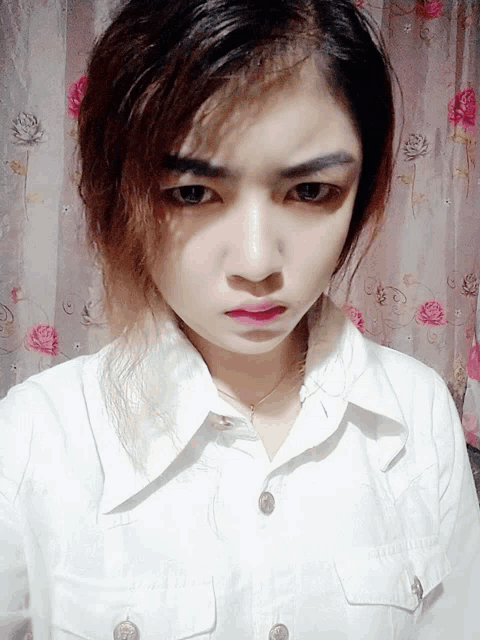 a woman wearing a white shirt with buttons on the front looks at the camera