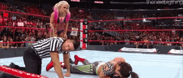 a female wrestler is standing on top of a referee in a wrestling ring .