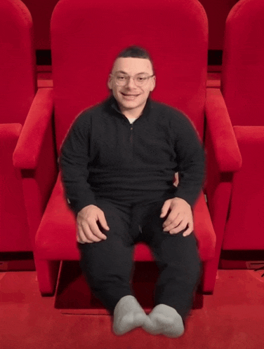 a man sits in a red chair with his legs crossed