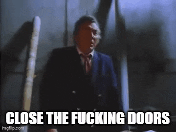 a man in a suit and tie is standing in a dark room with the words `` close the fucking doors '' written below him .