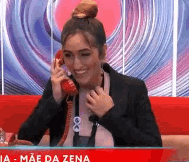 a woman is sitting on a couch talking on a red telephone .