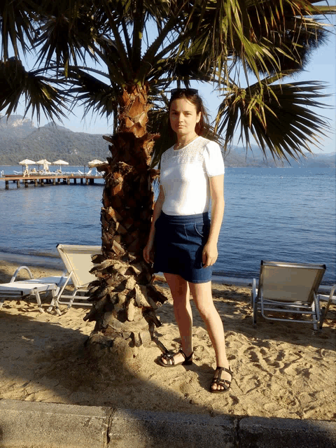 a woman standing under a palm tree on the beach