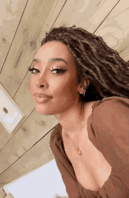 a woman with dreadlocks is wearing a brown shirt and a necklace