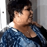 a woman wearing a blue shirt and hoop earrings is sitting on a couch .