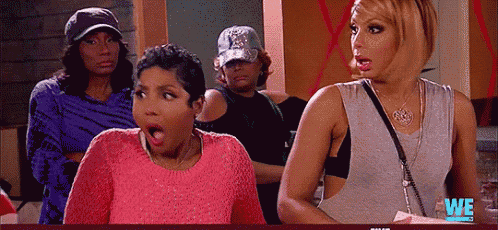 a group of women are standing in a room and one of them is wearing a pink sweater