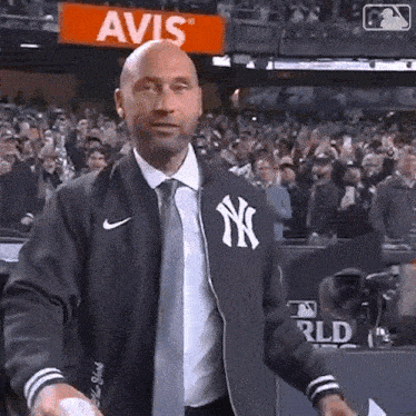 a man wearing a new york yankees jacket and tie is throwing a baseball in front of a crowd .