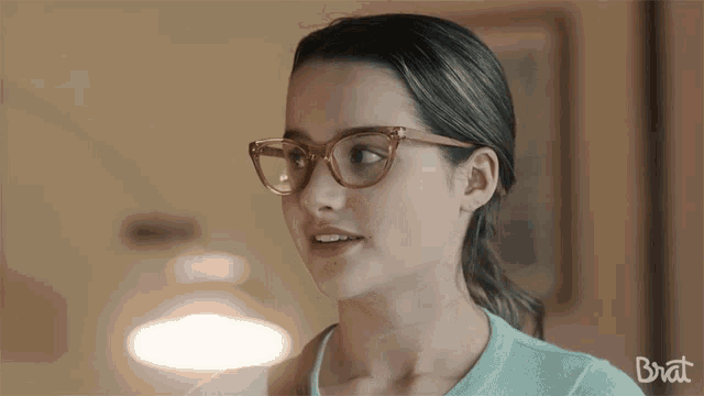 a woman wearing glasses and a blue shirt with the word brat on the bottom
