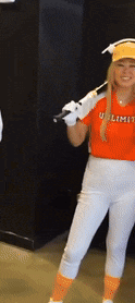a woman in an orange shirt that says unlimited holds a baseball bat