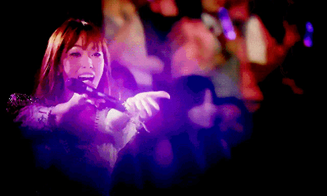 a woman singing into a microphone with a purple background