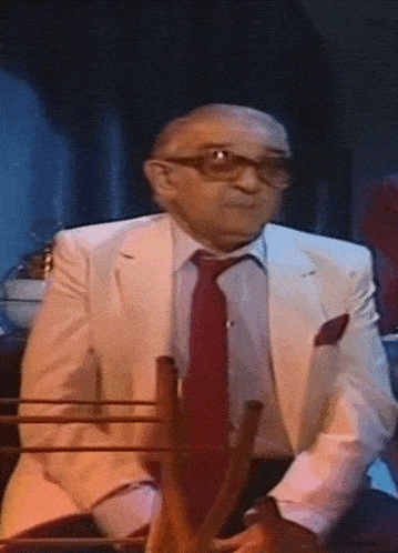 a man in a white suit and red tie is sitting in a chair