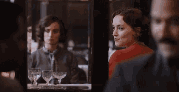 a woman is looking at her reflection in a mirror while a man looks on .