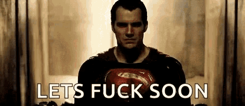 a man in a superman costume is standing in a hallway with the words `` lets fuck soon '' written on the screen .