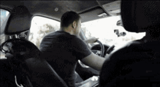 a man is driving a car with another man sitting in the back seat .