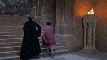 a woman in a pink blanket is walking down a set of stairs next to a man in a black robe