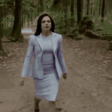 a woman in a light blue suit and skirt is walking through a forest .