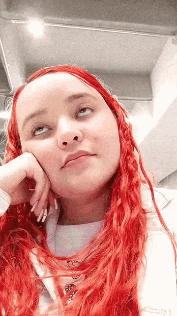 a woman with red hair and a white shirt has her hand on her face