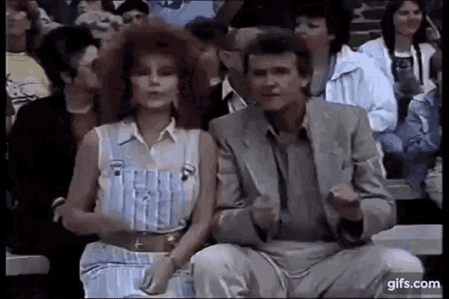 a man and a woman are sitting in a crowd of people . the woman has red hair and the man is wearing a suit .