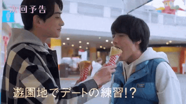 a man is feeding another man a crepe in a mall