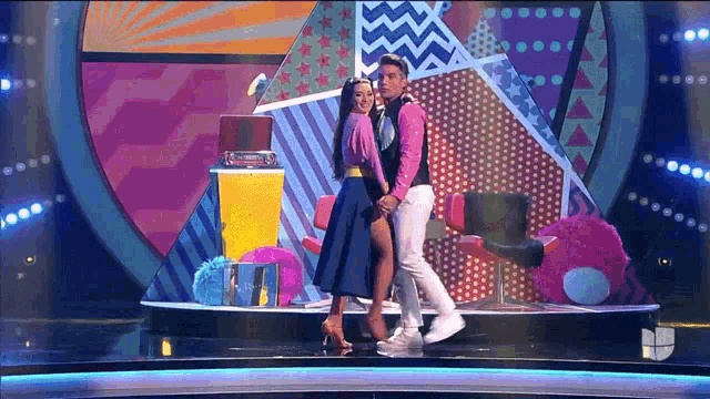 a man and woman are dancing on a stage with a colorful background