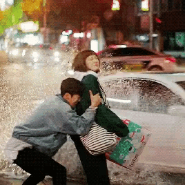 a man is carrying a woman in a puddle of water while a car is behind them