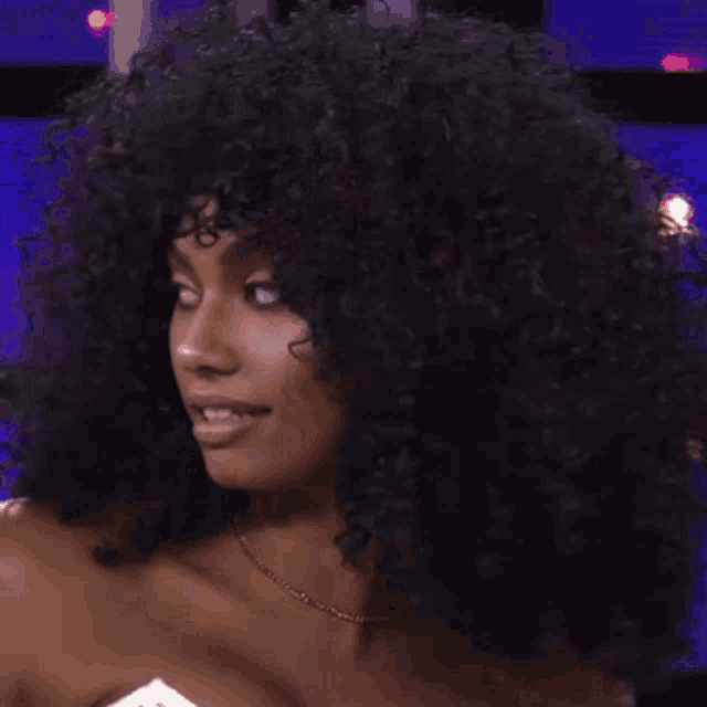 a woman with curly hair is wearing a gold necklace