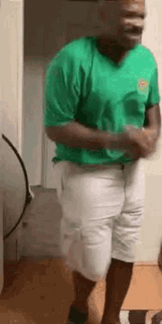 a man in a green t-shirt and white shorts is dancing in a room .