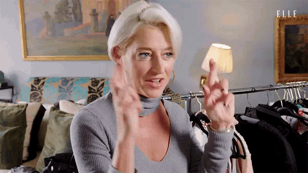 a woman in a grey sweater is giving the middle finger in front of a painting that says elle