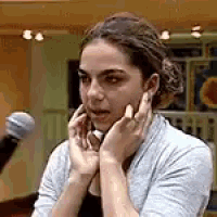 a woman is talking on a cell phone while holding her hands to her face in front of a microphone .