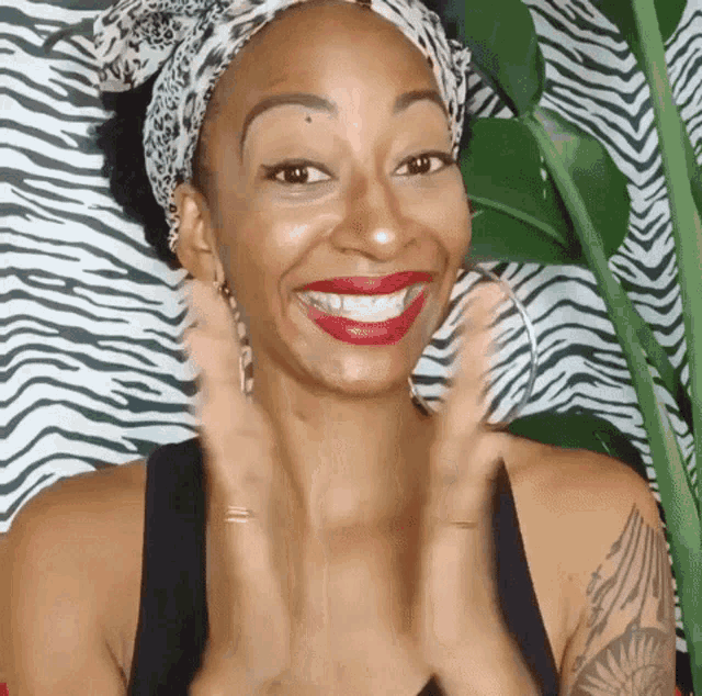 a woman wearing a headband and hoop earrings is smiling and clapping her hands in front of a zebra print wall .