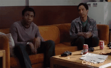 two men sit on a couch in front of a table with a can of coca cola on it