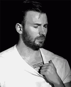 a man with a beard and a tattoo on his chest is taking off his shirt in a black and white photo .