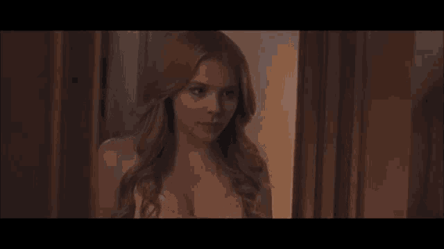 a woman in a bra is standing in a doorway looking out a window .