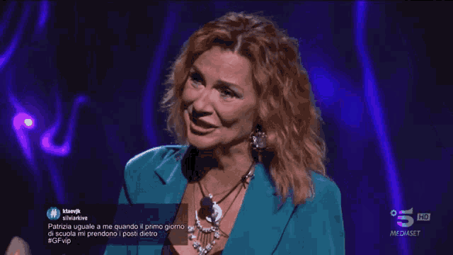 a woman in a blue jacket and necklace is on a tv screen