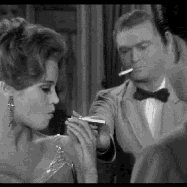 a woman in a dress is smoking a cigarette while a man in a tuxedo looks on