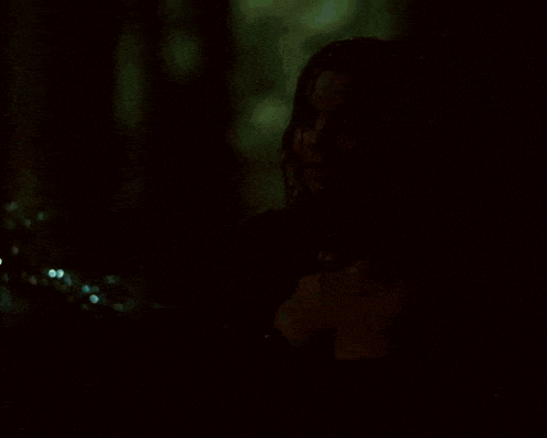 a woman in a black dress with a plunging neckline stands in the rain