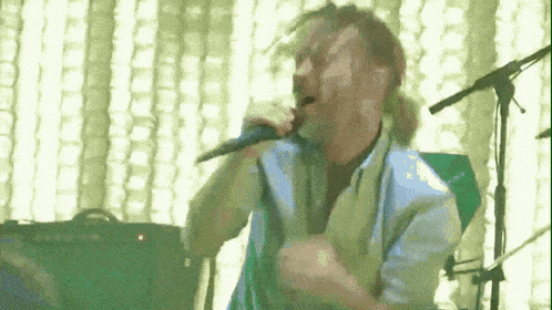 a man is singing into a microphone while sitting on a stage .