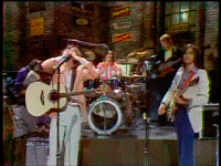 a man singing into a microphone while playing a guitar in front of a drum set
