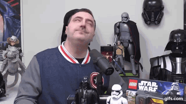 a man is standing in front of a microphone holding a darth vader action figure .