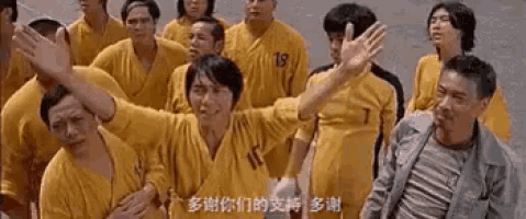 a group of men in yellow shirts are standing next to each other and waving at the camera .