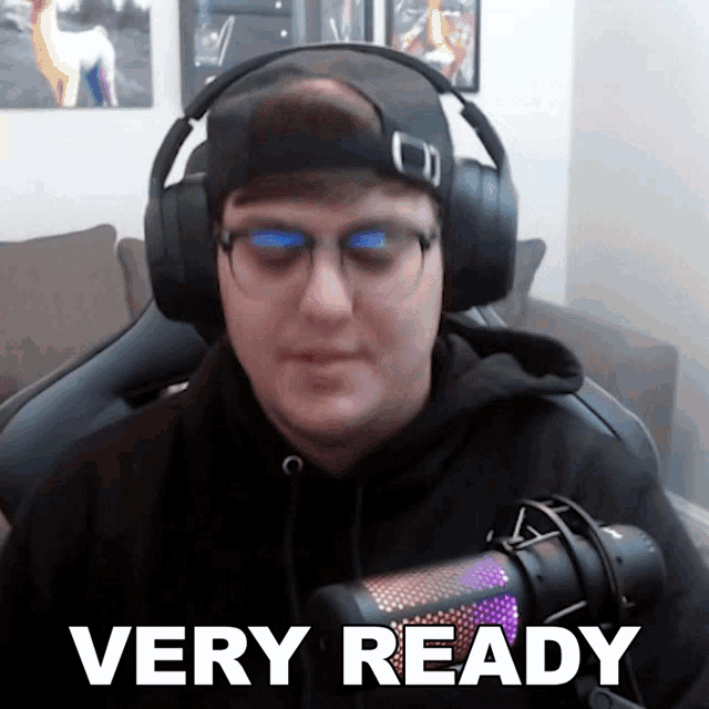 a man wearing headphones and glasses is sitting in front of a microphone and says very ready