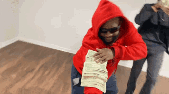 a man in a red hoodie holding a stack of money