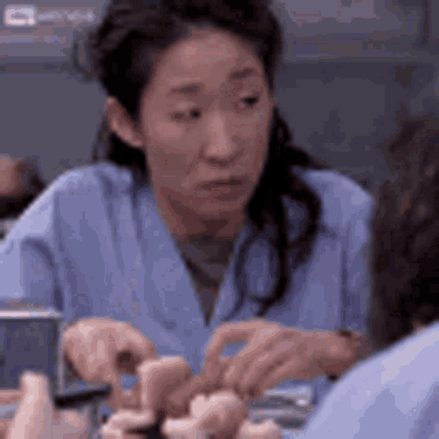 a woman in a blue scrub top is sitting at a table with her hands on a piece of food .