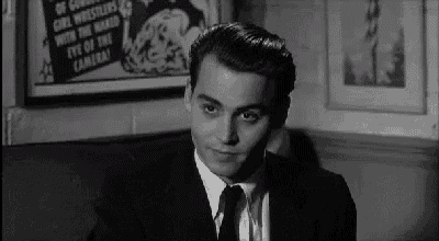a man in a suit and tie is sitting in a chair in front of a movie poster .