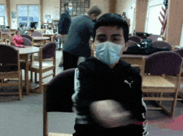 a boy wearing a mask and a puma jacket in a classroom
